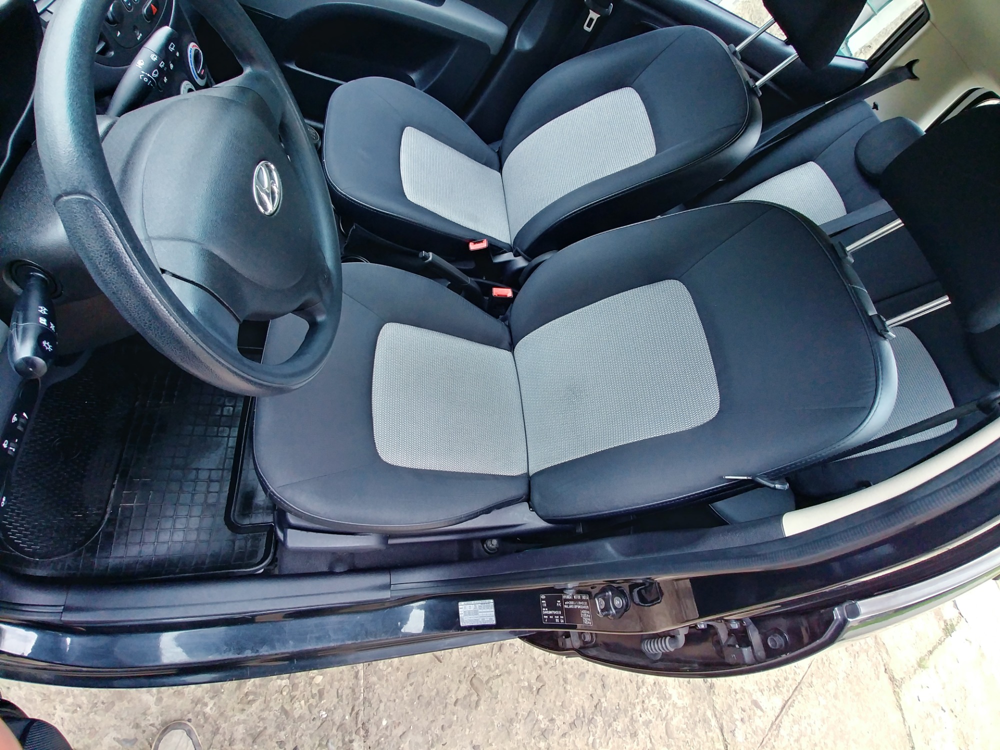 Wnętrze samochodu z czarno-szarymi siedzeniami i gumowymi dywanikami, widoczne z zewnątrz przez otwarte drzwi w Łączce.