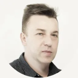 Portret mężczyzny z krótkimi włosami w ciemnej koszuli w kropki na jasnym tle. Ujęcie od przodu, skupione na twarzy. Drobne zmarszczki wokół oczu.