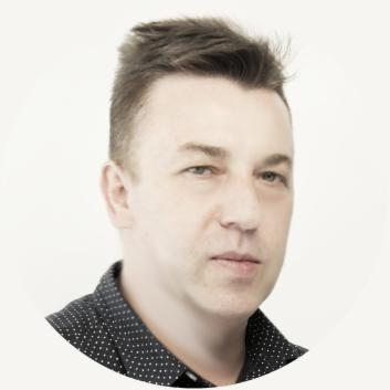 Portret mężczyzny z krótkimi włosami w ciemnej koszuli w kropki na jasnym tle. Ujęcie od przodu, skupione na twarzy. Drobne zmarszczki wokół oczu.