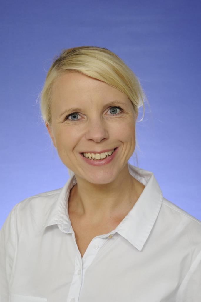 Portret uśmiechniętej blondynki w białej koszuli na niebieskim tle, prezentujący profesjonalizm copywritera.