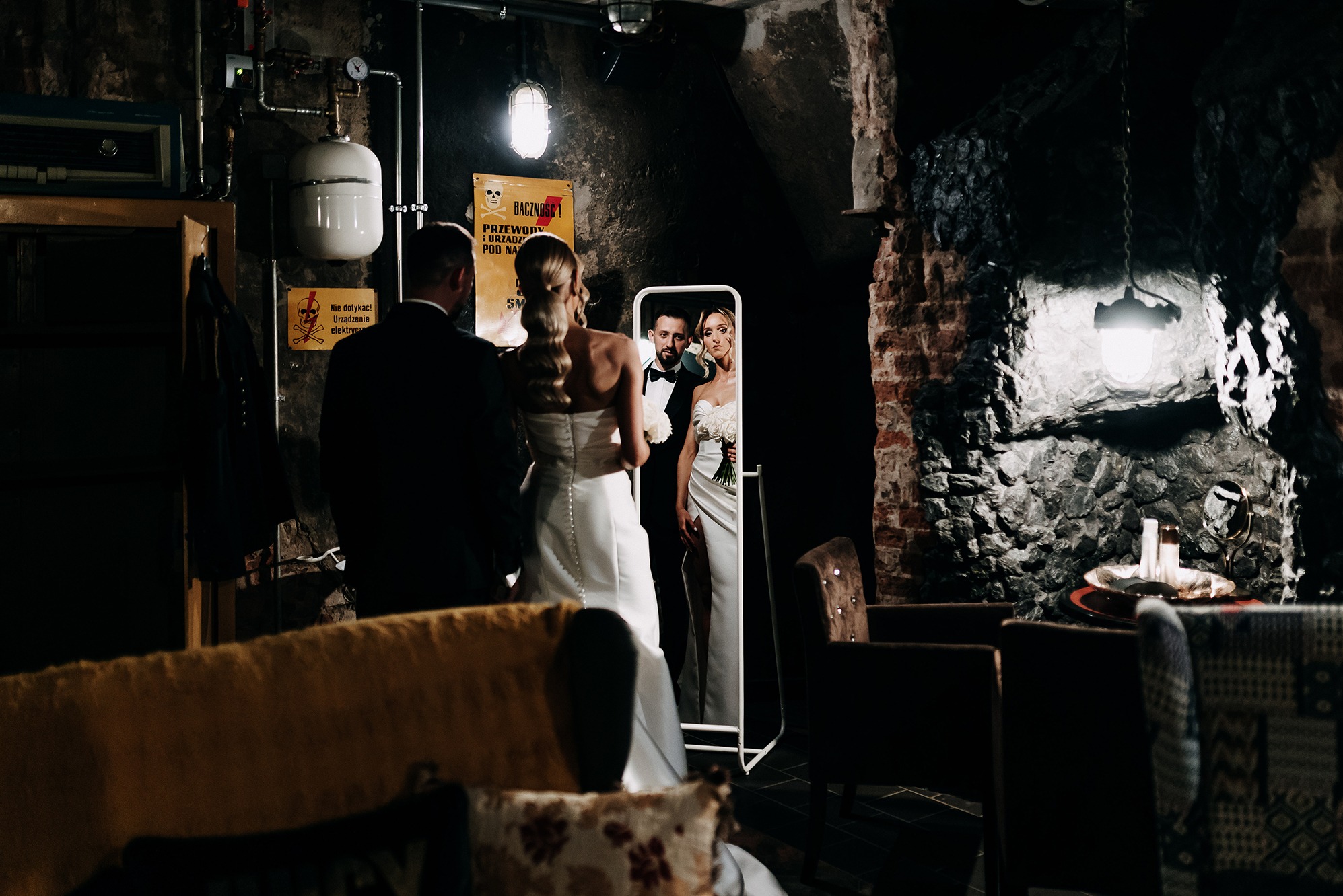 Para młoda w industrialnym wnętrzu, odbicie w lustrze. Nietypowa sceneria ślubna z surowymi ścianami i dekoracjami. Nowoczesne ujęcie fotografii ślubnej.