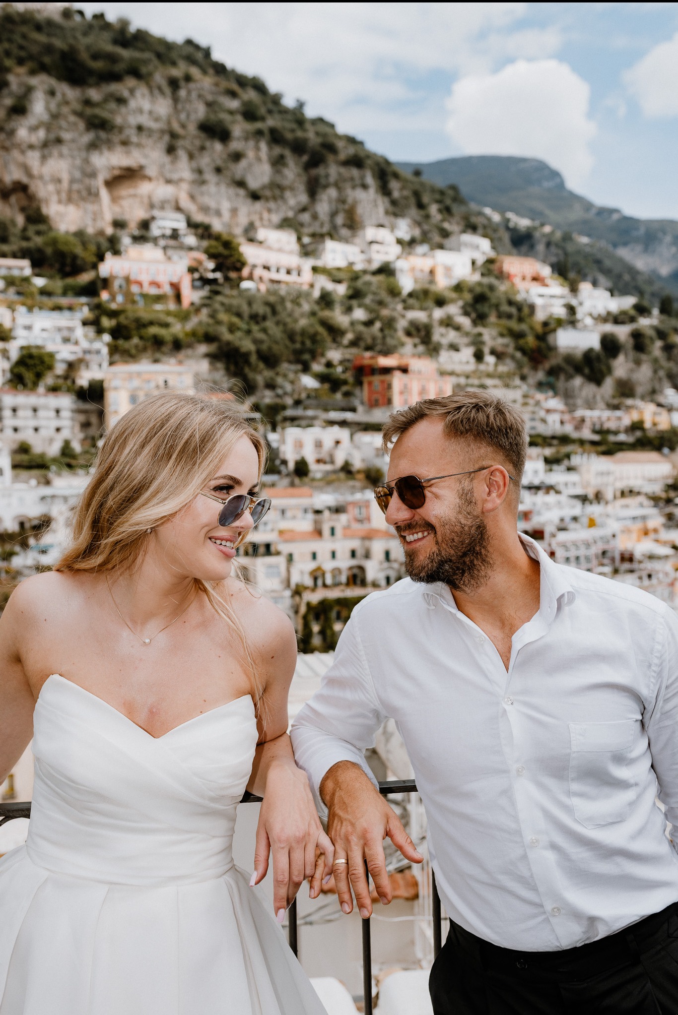 Para młoda w Lublinie, w okularach przeciwsłonecznych, opiera się o barierkę z widokiem na malownicze miasto na wzgórzu. Uśmiechnięci, w jasnych strojach.