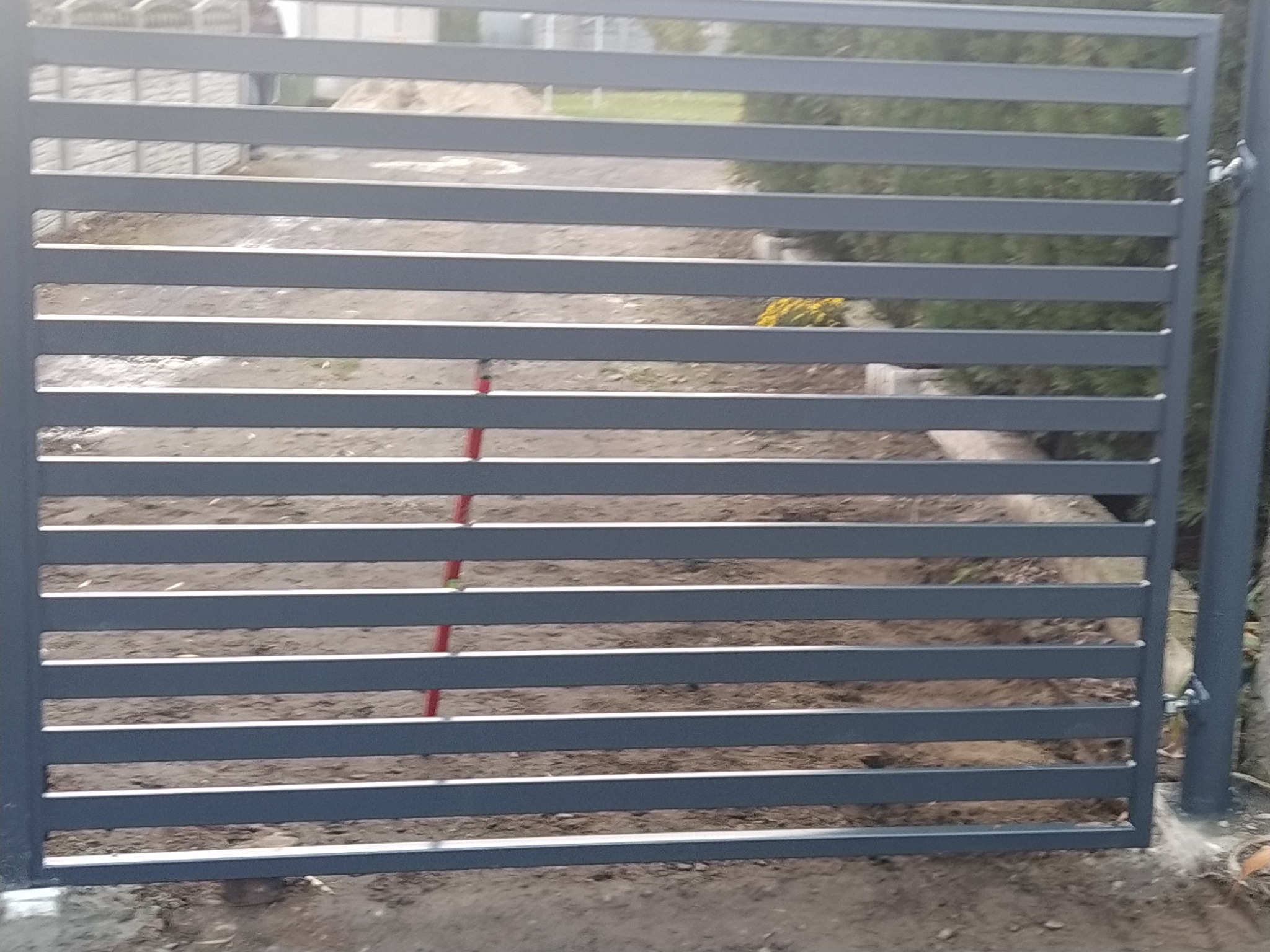 Nowoczesna, metalowa brama posesyjna z poziomymi szczeblami, świeżo zamontowana na gruncie.