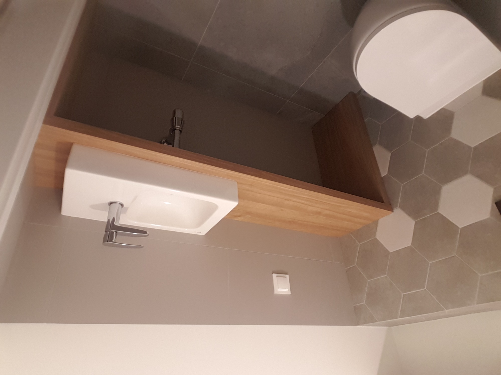 Nowoczesna łazienka z umywalką nablatową na drewnianym blacie, heksagonalne płytki na ścianie i wisząca toaleta.