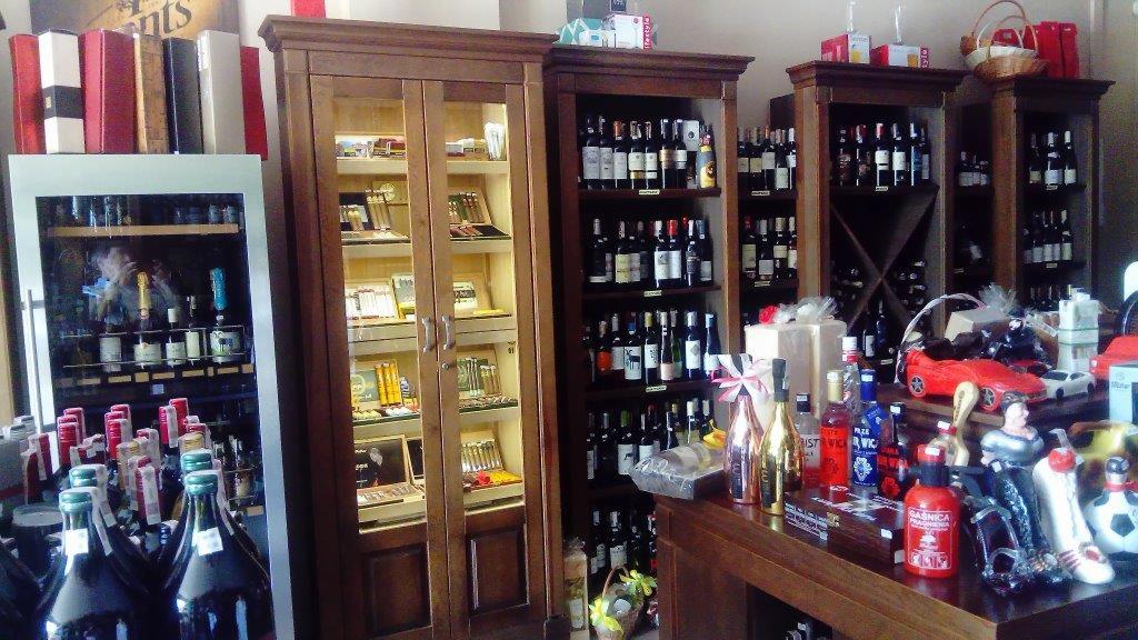 Wnętrze sklepu w Warszawie z alkoholem i cygarami, widoczne regały z butelkami wina i szafka ekspozycyjna z cygarami, na pierwszym planie dekoracje i butelki alkoholu na drewnianym blacie.