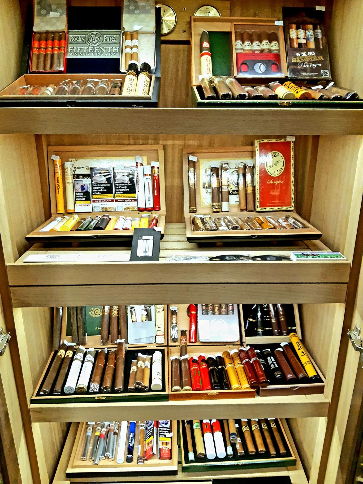 Szafa humidora wypełniona różnorodnymi cygarami różnych marek i formatów, ułożonymi w drewnianych pudełkach i ekspozytorach.
