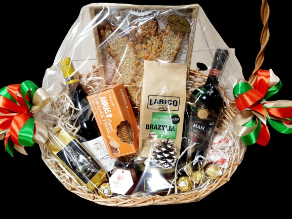 Kosz upominkowy z winem, kawą, ciastkami i miodem, zapakowany w przezroczysty celofan i ozdobiony czerwoną oraz zieloną wstążką.
