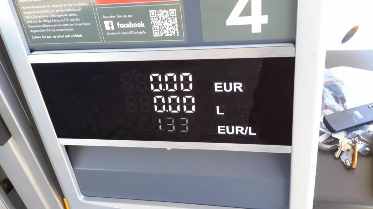 Wyświetlacz dystrybutora paliwa na stacji benzynowej z zerowymi wartościami EUR i L oraz ceną 1.33 EUR/L, obok leżą klucze i pilot.
