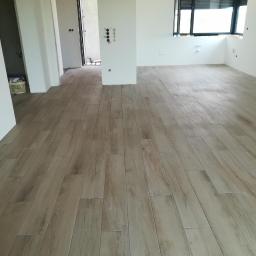 Darioremonty - Ułożone panele podłogowe imitujące drewno w jasnym, pustym pomieszczeniu z białymi ścianami i oknem z żaluzjami.