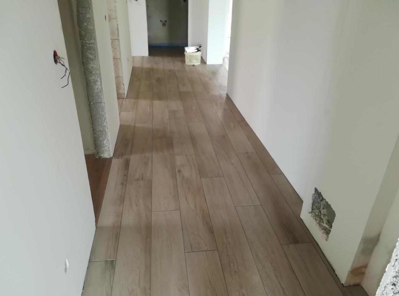 Korytarz w trakcie wykańczania: ułożona podłoga z paneli imitujących drewno, ściany w trakcie malowania, widoczne niedokończone fragmenty i instalacje elektryczne.