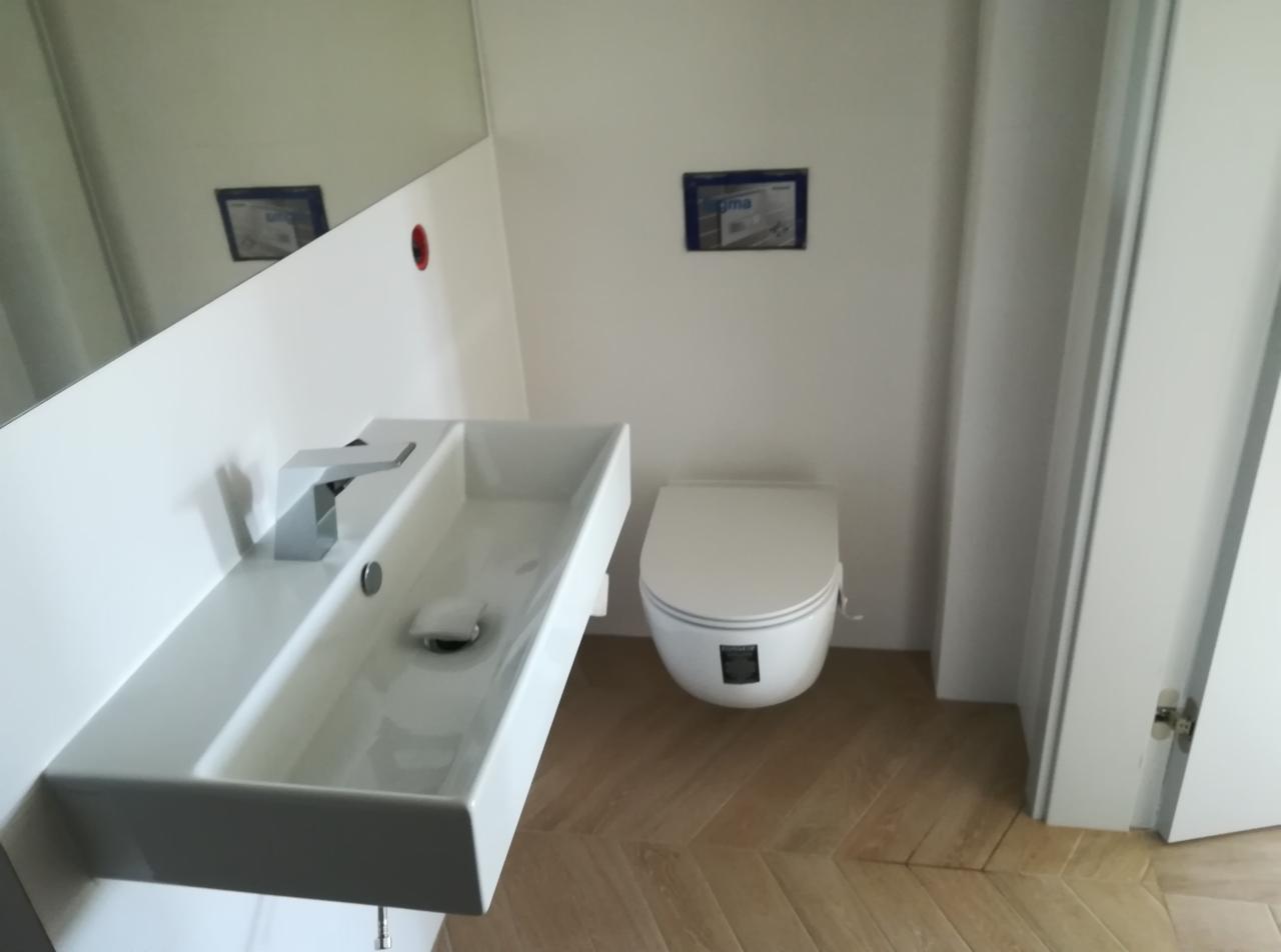 Nowoczesna łazienka z wiszącą, prostokątną umywalką z chromowaną baterią, podwieszanym WC i podłogą z parkietu ułożonego w jodełkę.