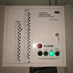 Panel sygnalizacyjny zalania wodą IBS-TSOA17B z diodami wskazującymi poziom zalania w wieżach A i B, przyciskami sygnalizacji, wyciszenia i wyłącznikiem oraz kluczem w zamku.