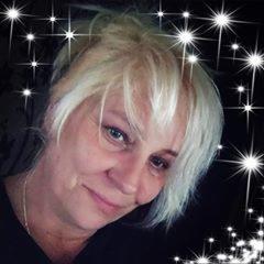 Portret kobiety z krótkimi blond włosami, lekko uśmiechniętej, na ciemnym tle z efektem rozbłyskujących gwiazd.