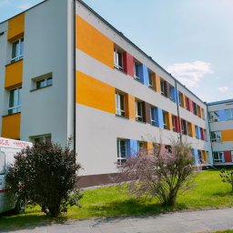 Danplex Michał Danilczyk - Odnowiona elewacja budynku szkolnego z kolorowymi pasami i obramowaniami okien, widoczny firmowy bus z napisem 'Elewacje Wnętrza'.