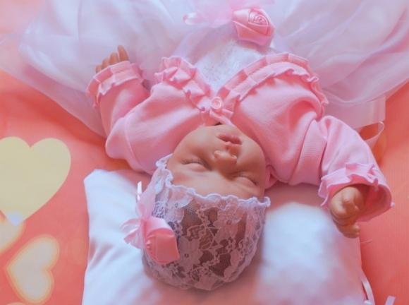 Śpiące niemowlę w różowej sukience z falbankami i koronkowym czepku na białej poduszce z różowymi akcentami w kształcie serc.