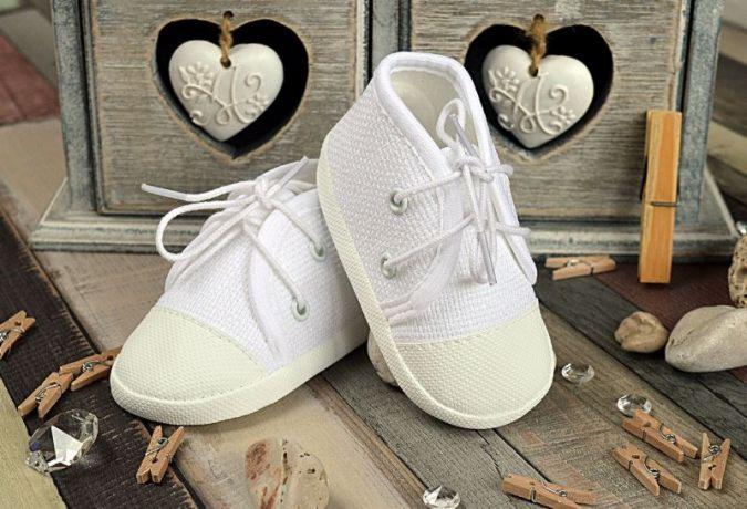 Dwa białe, sznurowane buciki niemowlęce na drewnianym tle z ozdobnymi sercami i miniaturowymi klamerkami.
