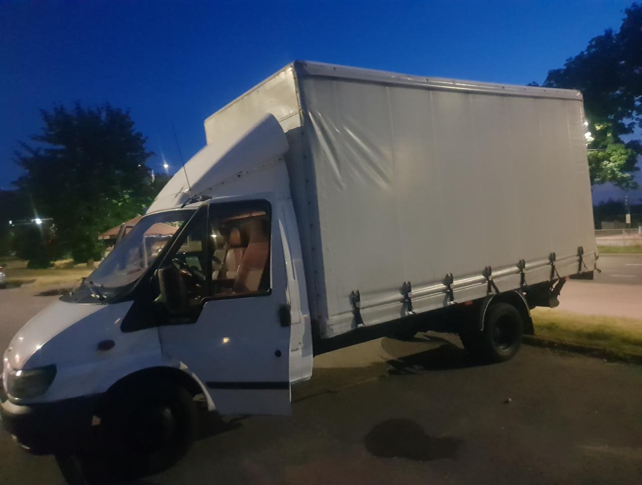 Biały samochód dostawczy z otwartymi drzwiami kierowcy, zaparkowany na parkingu o zmierzchu, widoczne brązowe fotele w kabinie.