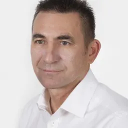 Portret mężczyzny w białej koszuli na jasnym tle. Widoczna krótka fryzura i wyraz twarzy sugerujący profesjonalizm.