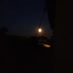 Nocny krajobraz z widocznym oświetleniem budynku w oddali, sfotografowany w słabych warunkach oświetleniowych.