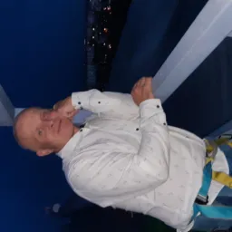 Mężczyzna w uprzęży, na wysokości, prawdopodobnie podczas prac remontowych. Widoczne elementy konstrukcji i nocny krajobraz w tle. Ujęcie z dołu.