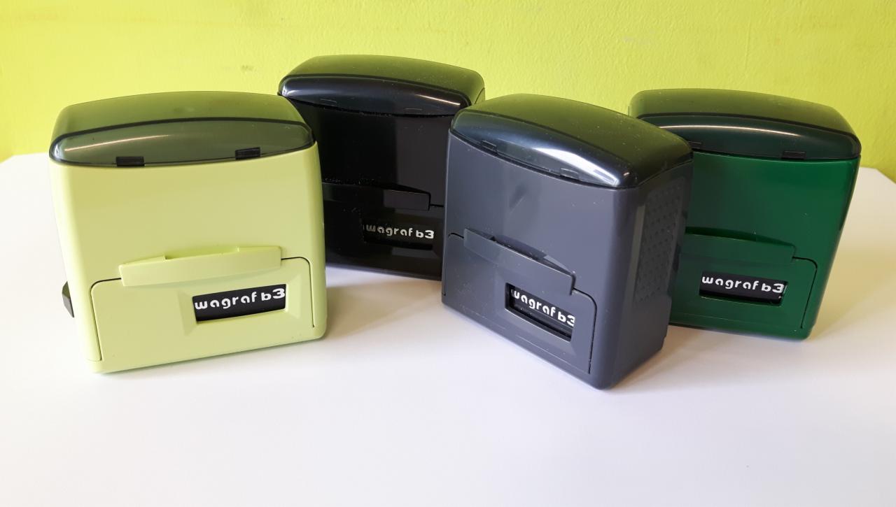 Cztery automatyczne stemple w kolorach: pistacjowym, czarnym, szarym i zielonym, ustawione obok siebie na białym blacie, z widocznym napisem 'wagraf b3' na każdym z nich.