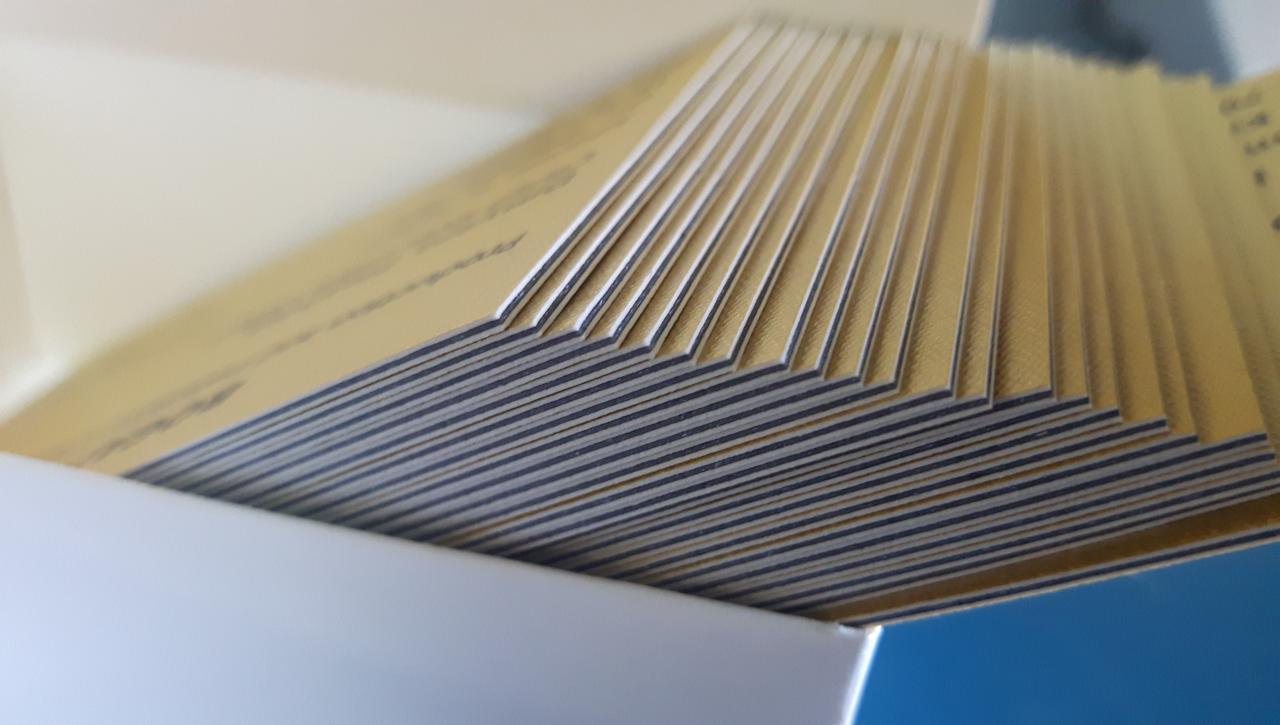 Stos wizytówek z pozłacanymi brzegami, ułożonych w pudełku, widoczne krawędzie z ciemnym nadrukiem.