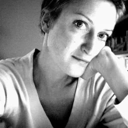 Portret kobiety z krótkimi włosami, opierającej brodę na dłoni, w czarno-białej tonacji, z półką na książki w tle.