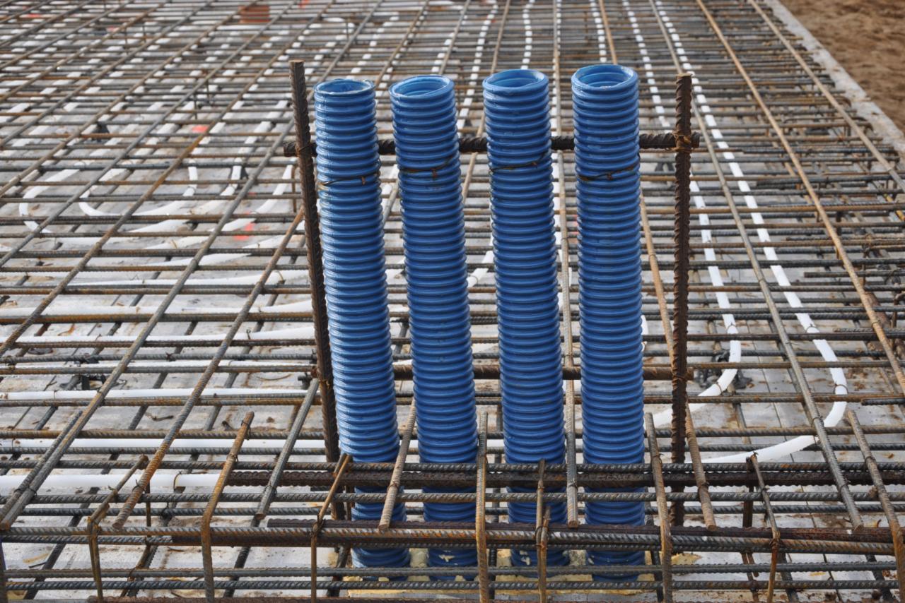 Zbrojenie fundamentu z pionowo wystającymi, niebieskimi rurami karbowanymi, zabezpieczonymi drutem wiązałkowym.