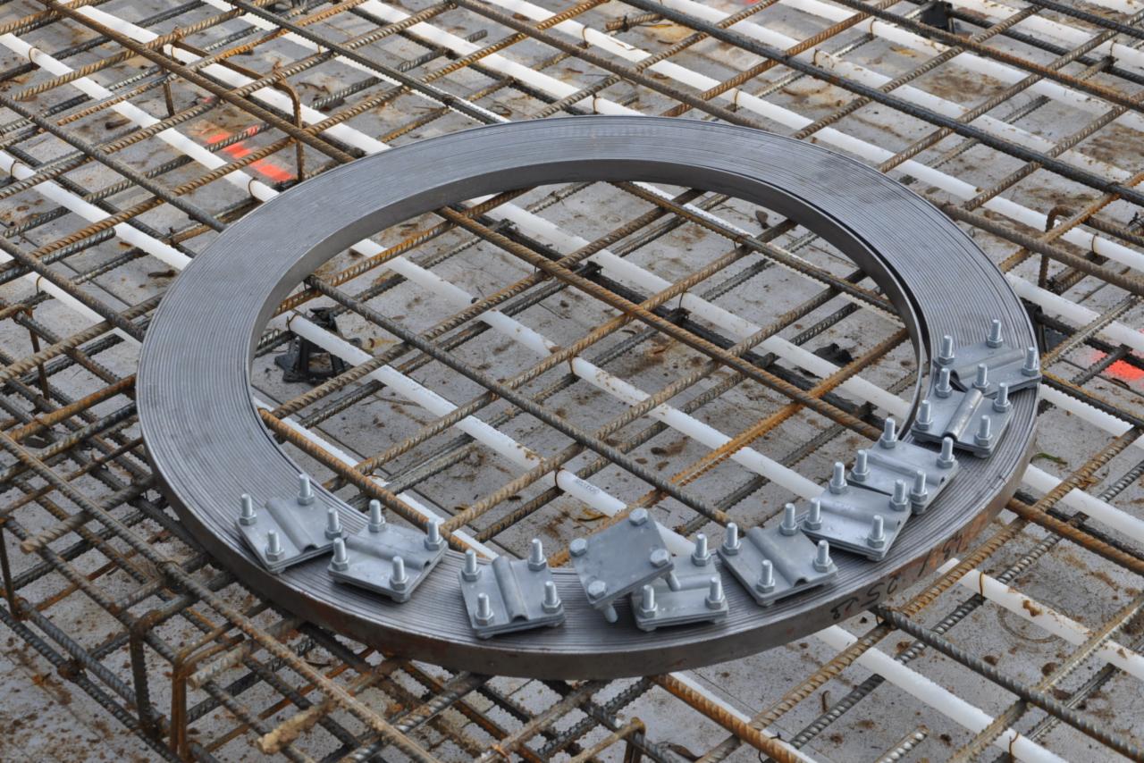 Okrągła, stalowa forma z zamocowanymi klamrami na siatce zbrojeniowej, widok z góry, przygotowanie do zalewania betonem.