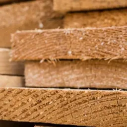 Stos świeżo przetartego drewna o widocznych słojach, ułożonego równo w stos, z drobnymi wiórami na powierzchni cięcia.