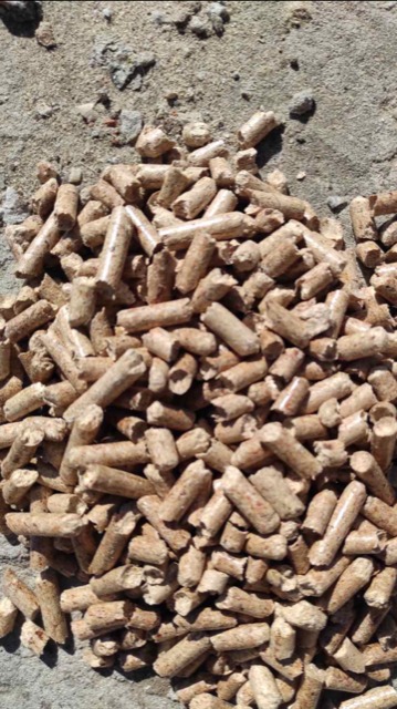Stos brązowych, cylindrycznych peletek z widocznymi śladami trocin na szarym, betonowym podłożu.
