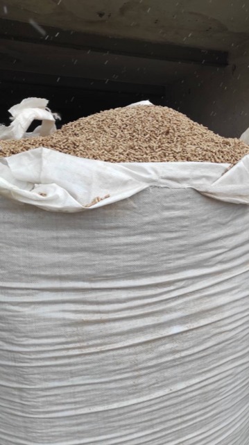 Worek typu Big Bag wypełniony jasnymi, drobnymi granulkami paliwa stałego na tle betonowej ściany. Widoczne ślady wilgoci na worku.