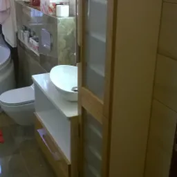 Nowoczesna łazienka z umywalką nablatową na szafce z otwartą półką i wysoką szafą z przeszklonymi drzwiczkami, widok z boku.