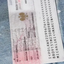 Zdjęcie polskiego dowodu osobistego na tle dżinsowej tkaniny. Widoczne dane osobowe, w tym imię, nazwisko, PESEL i data ważności dokumentu. Ujęcie z bliska, lekko obrócone.