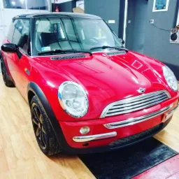 Czerwony Mini Cooper z czarnym dachem na podnośniku w warsztacie samochodowym, widok z przodu, lekki kąt z lewej strony.