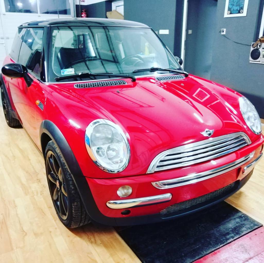 Czerwony Mini Cooper z czarnym dachem na podnośniku w warsztacie samochodowym, widok z przodu, lekki kąt z lewej strony.
