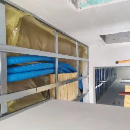 Konstrukcja metalowa sufitu podwieszanego z izolacją z wełny mineralnej i niebieskimi rurami instalacyjnymi w przestrzeni między sufitem a płytą gipsową, widok z dołu.