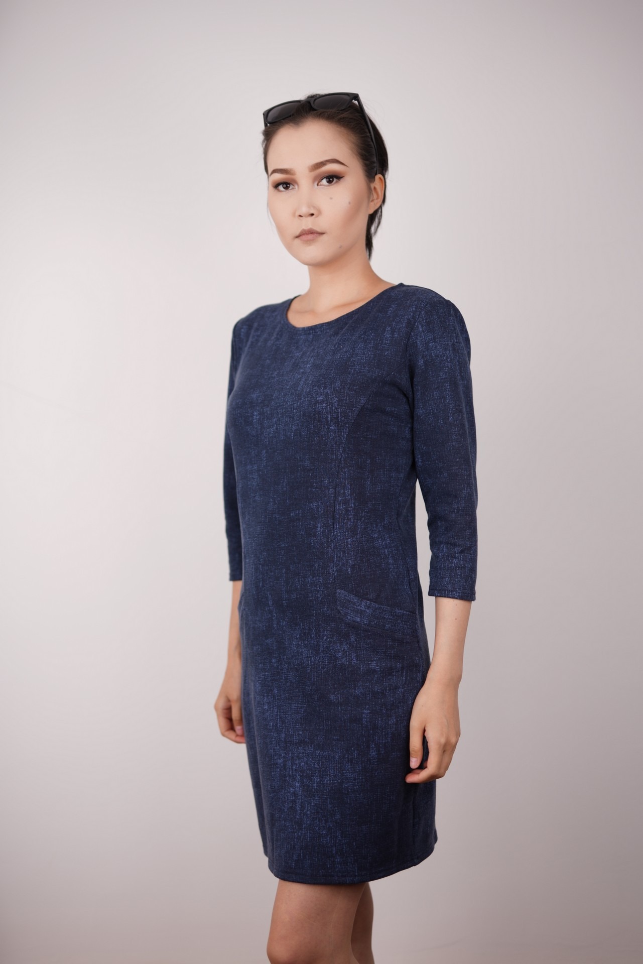 Kobieta prezentuje granatową sukienkę z rękawem 3/4 i kieszenią, na białym tle.