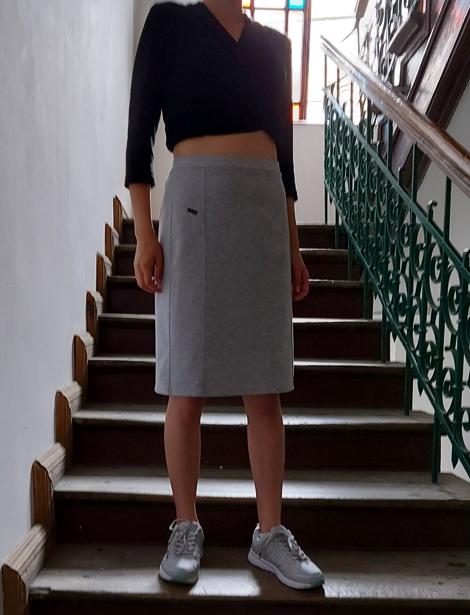 Osoba w czarnym topie i szarej spódnicy na schodach z ozdobną balustradą, prezentacja gotowego wyrobu.