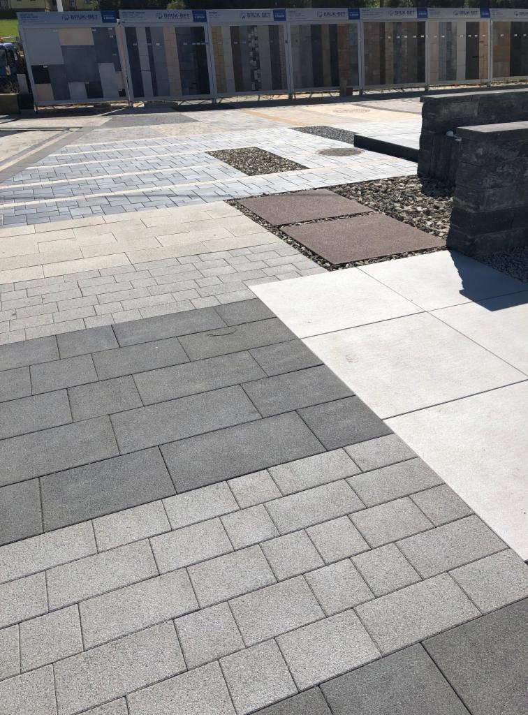 Ekspozycja różnorodnych wzorów i kolorów nawierzchni z kostki brukowej oraz płyt betonowych na terenie składu budowlanego w Spytkowicach, prezentująca aranżacje z wykorzystaniem kamieni ozdobnych.