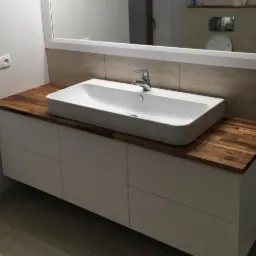 Nowoczesna łazienka z białą szafką pod umywalkę, blatem z drewna egzotycznego i prostokątną umywalką nablatową.