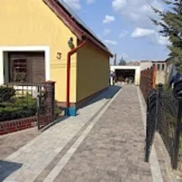 Ułożony chodnik z szarej kostki brukowej z dwoma pasami z ciemniejszej kostki, prowadzący od furtki do budynku mieszkalnego z numerem 3, widok z poziomu gruntu.