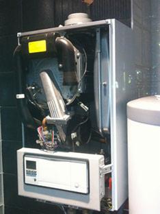 Otwarty kocioł grzewczy z widocznymi elementami wewnętrznymi, w tym palnikiem i okablowaniem, obok biały zasobnik ciepłej wody.