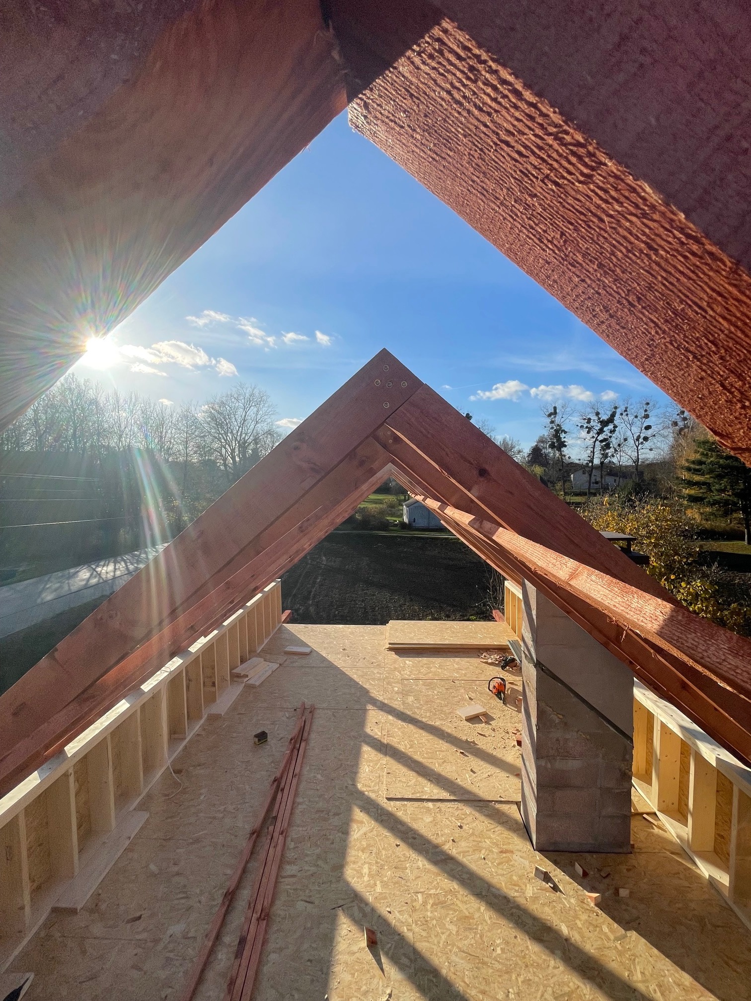 Wnętrze domu w trakcie budowy, widoczna drewniana konstrukcja dachu i ścian, jasne światło słoneczne wpadające przez otwór w dachu, perspektywa od dołu.