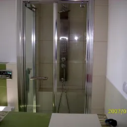 Szklana kabina prysznicowa z panelem natryskowym w wykończonej łazience, widok na baterię i toaletę w tle, data na zdjęciu wskazuje na rok 2007.