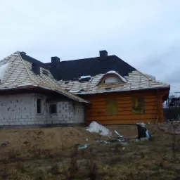 Budowa domu: część murowana z pustaków i część drewniana w trakcie krycia dachu, widoczne rusztowania i materiały budowlane.