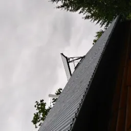 Panel solarny zamontowany na dachu domu z drewnianą elewacją, widok z dołu w pochmurny dzień.