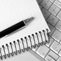 Notatnik ze spiralą i długopis leżące na klawiaturze komputera, zdjęcie czarno-białe.