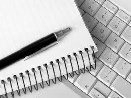 Notatnik ze spiralą i długopis leżące na klawiaturze komputera, zdjęcie czarno-białe.