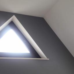 Dan-Bud - Szara ściana w pokoju na poddaszu z trójkątnym oknem i białym sufitem z wbudowanym oświetleniem.